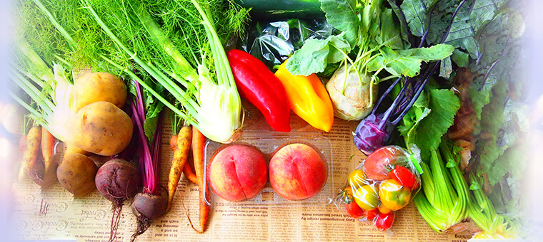 モモ、カブ、ニンジン、トマト、ジャガイモなどの野菜が英字模様の敷物の上に並べられている写真
